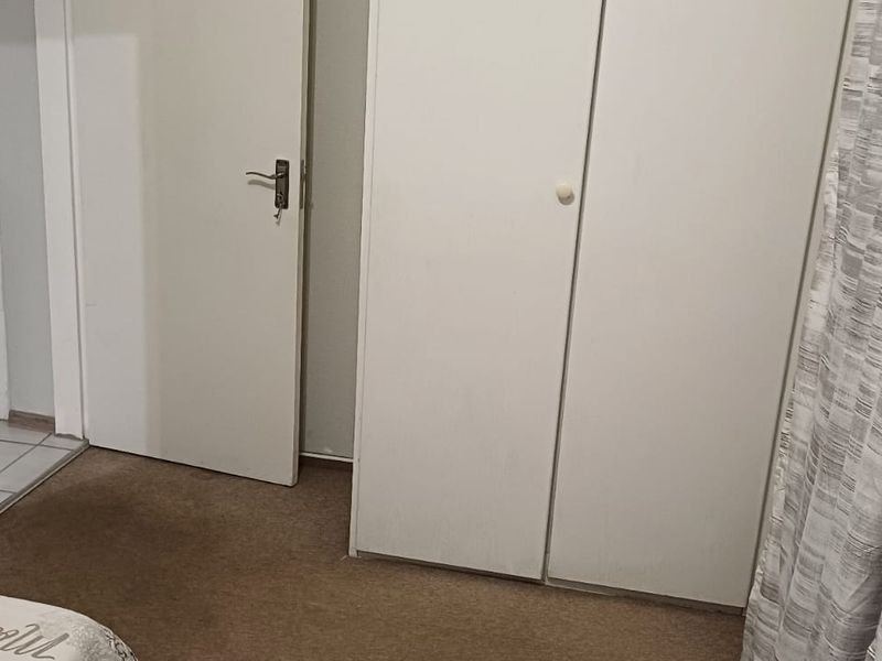 A bedroom featuring built-in wardrobe storage, carpeted flooring, and access to an adjacent hallway.