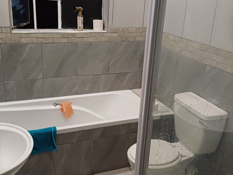 A functional bathroom featuring a bathtub, pedestal basin, toilet, and a separate shower enclosure with modern grey wall tiling.