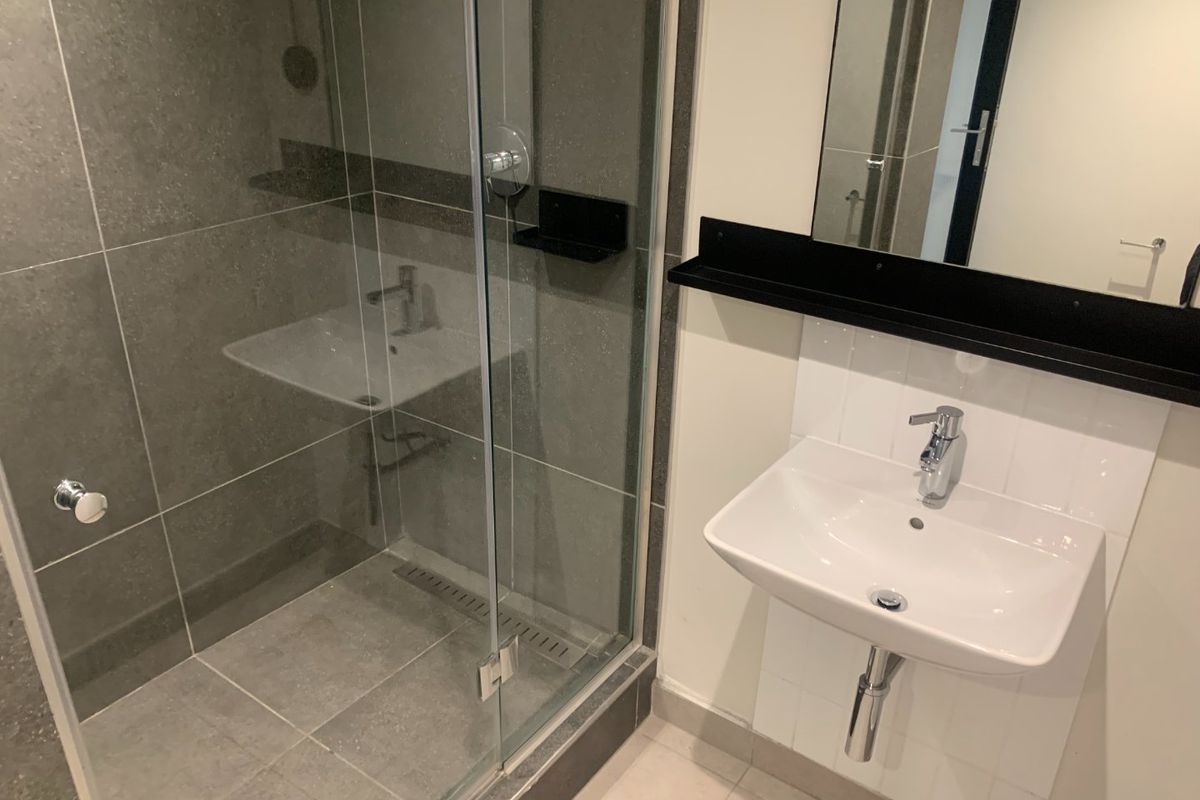 Modern bathroom featuring a glass-enclosed walk-in shower with grey tiling and a wall-mounted white ceramic basin with chrome fixtures.