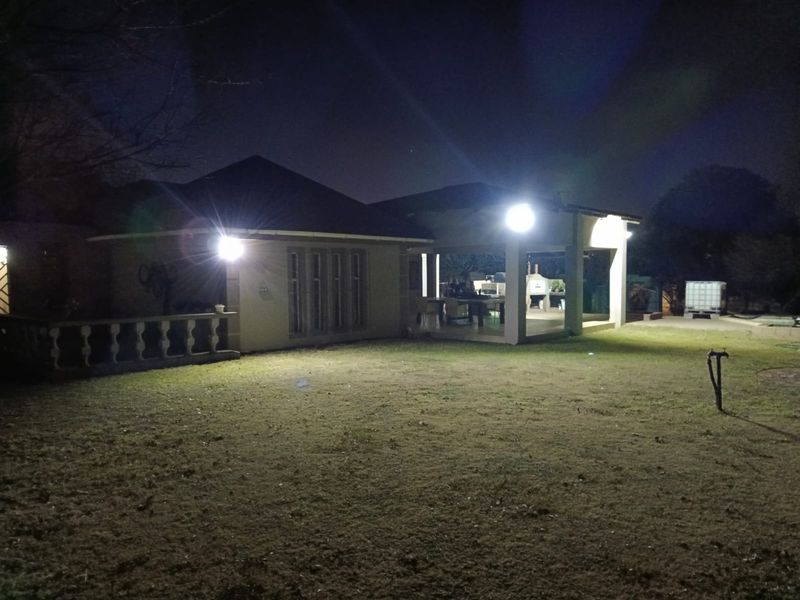 Night view of the rear exterior of the property, featuring a covered patio area and a spacious garden.