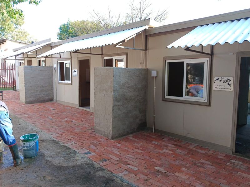 Exterior view of a row of modular units featuring brick paved walkways, corrugated metal awnings, and individual privacy walls.
