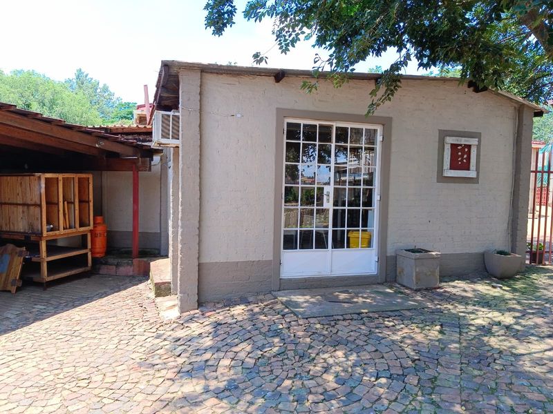 Exterior view of a small holding outbuilding featuring a French door entrance, paved courtyard area, and a covered side structure.