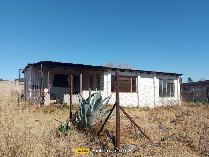 A small holding property featuring a single-story structure with a corrugated roof, requiring significant maintenance and renovation to restore its exterior condition.