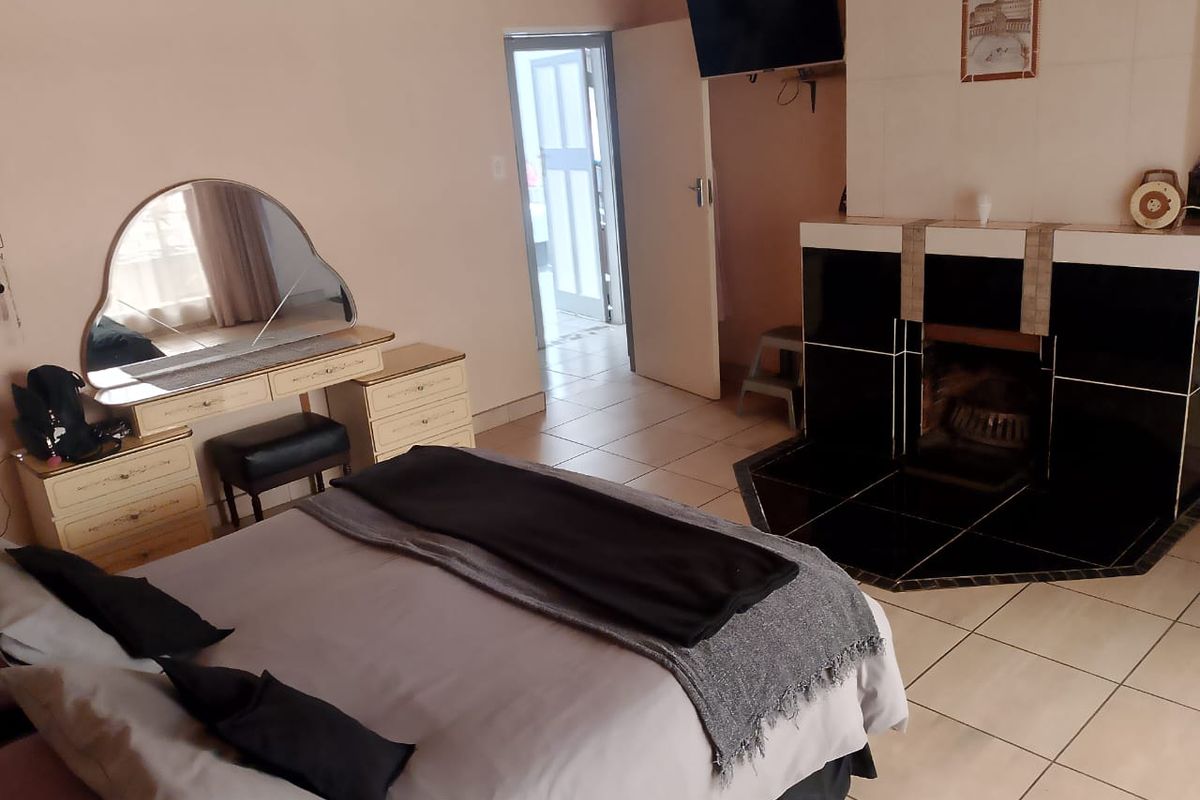 Spacious bedroom featuring tiled flooring and a built-in fireplace, providing a cozy atmosphere with direct access to an adjacent room.