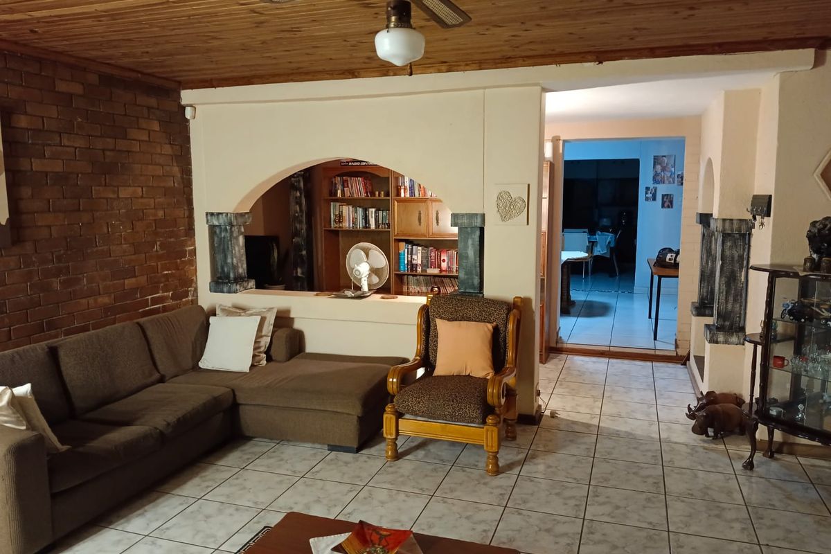 Spacious living area featuring a rustic brick feature wall, arched room divider, and timber-clad ceiling with a central fan.