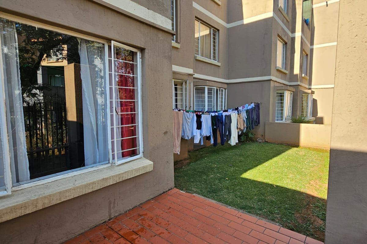 Rear view of the apartment building featuring a private brick-paved patio area and a small communal lawn space.