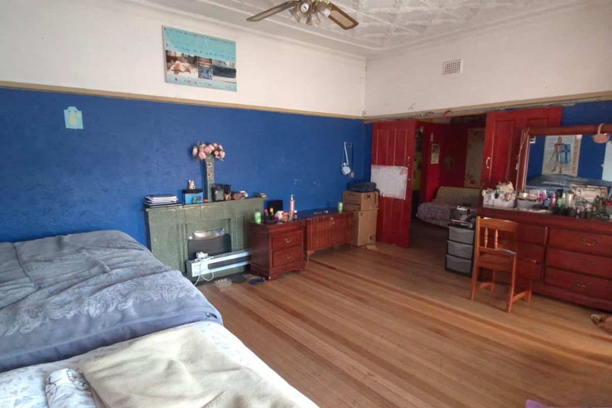 Spacious bedroom featuring original timber flooring, decorative ceiling detail, and a built-in fireplace, offering a classic layout with potential for modernization.