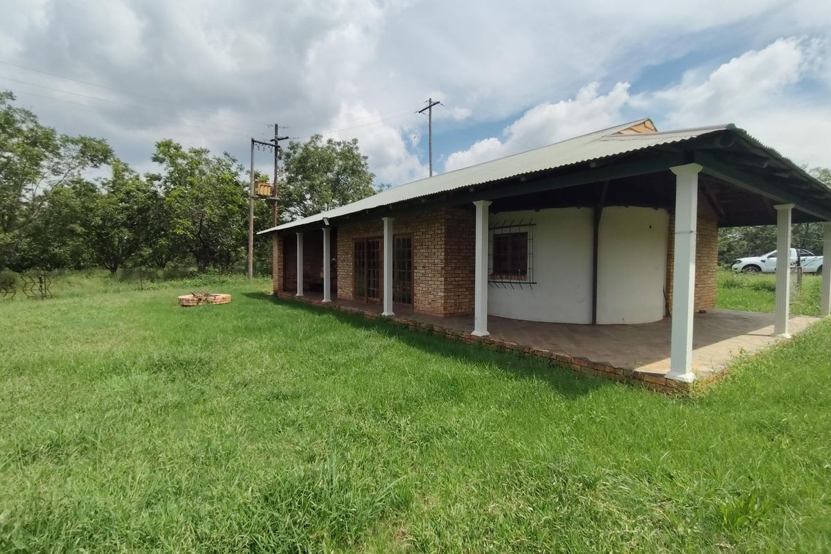 A rear view of a farm-style dwelling featuring a covered patio, brick exterior walls, and a metal roof set within a grassy landscape.