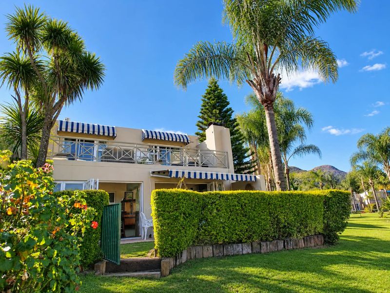 Rear view of the townhouse featuring a private garden, a spacious upper balcony with metal balustrades, and retractable awnings over the patio area.