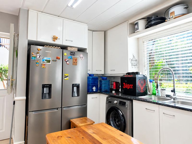 A functional kitchen featuring white cabinetry, dark granite countertops, a stainless steel sink with a gooseneck faucet, and an integrated washing machine.