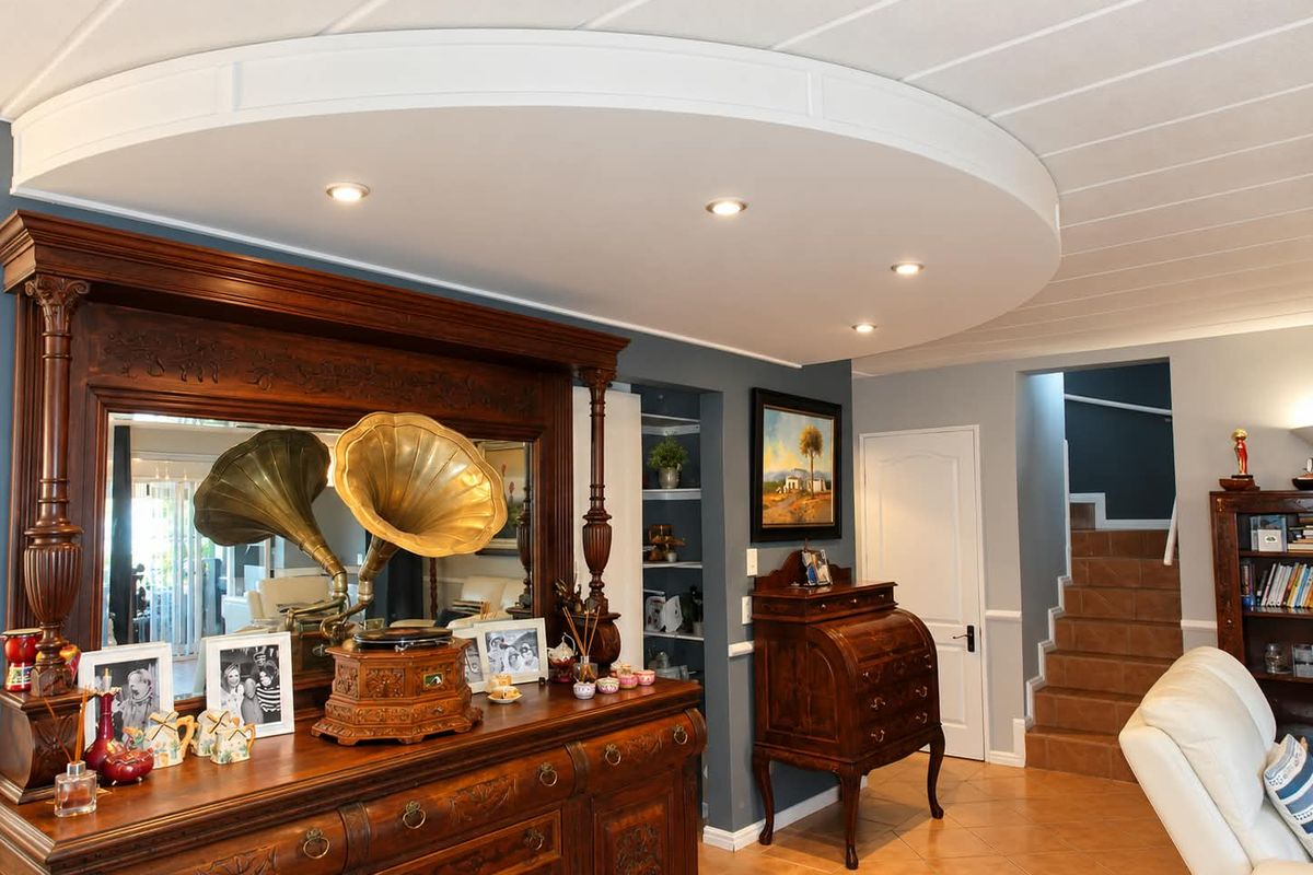 A well-maintained living area featuring a distinctive curved bulkhead ceiling with recessed lighting, tiled floors, and a staircase leading to the upper level.