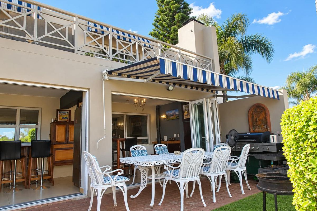 A spacious outdoor patio featuring brick paving, a retractable striped awning, and a built-in fireplace, seamlessly connected to the interior living area via folding doors.