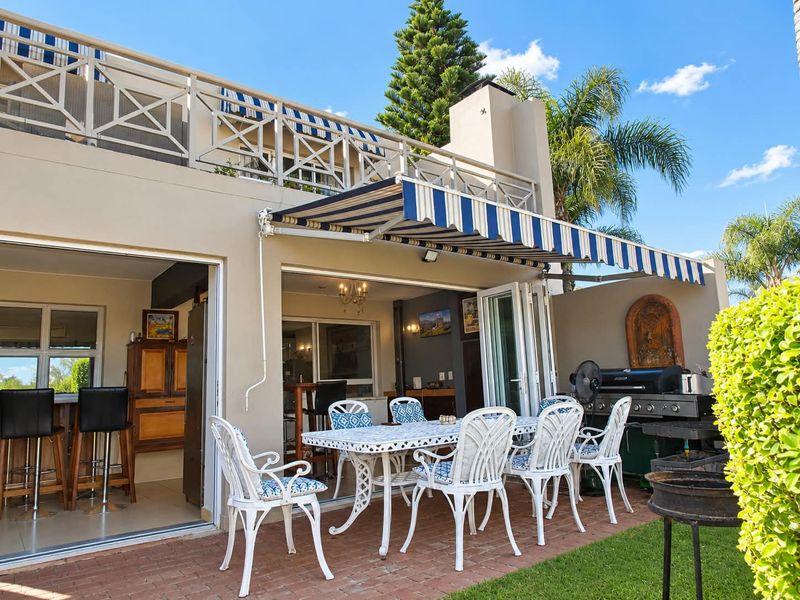 A spacious outdoor patio featuring brick paving, a retractable striped awning, and a built-in fireplace, seamlessly connected to the interior living area via folding doors.