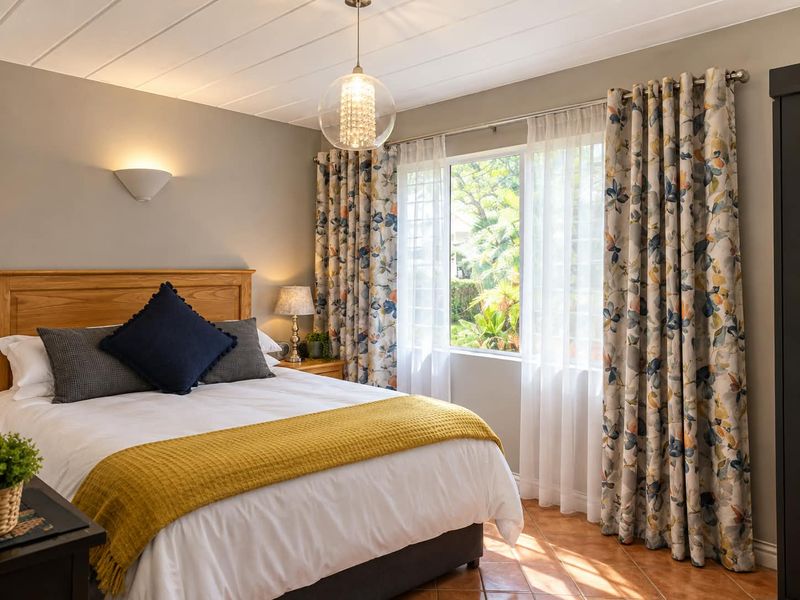 A well-maintained bedroom featuring tiled flooring, a panelled ceiling, and natural light through a large window with decorative curtains.