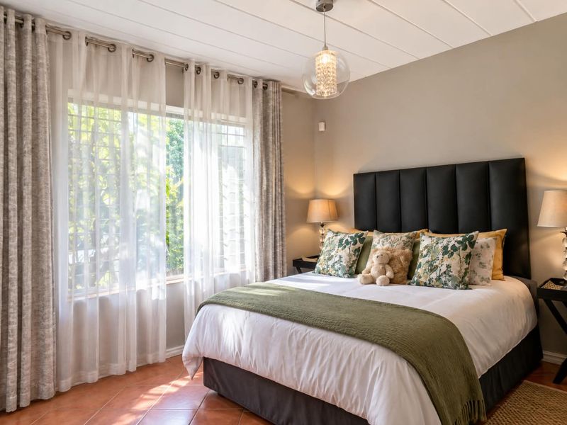A well-lit bedroom featuring tiled flooring, neutral wall tones, and a large window with security bars, creating a comfortable and inviting sleeping space.