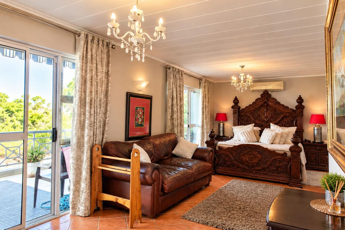 Spacious bedroom featuring tiled flooring, dual crystal chandeliers, split-system air conditioning, and sliding glass doors leading to a private balcony.