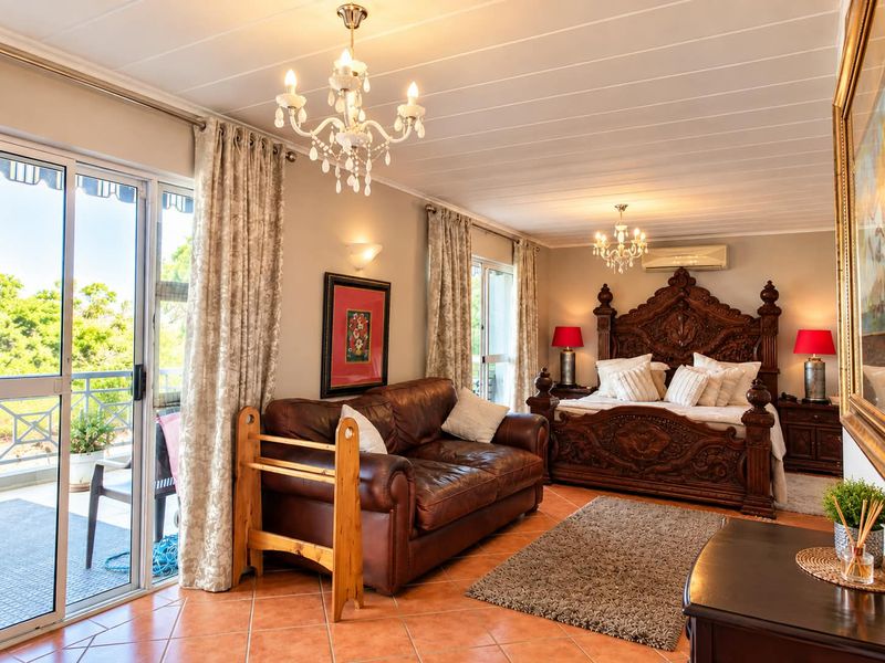 Spacious bedroom featuring tiled flooring, dual crystal chandeliers, split-system air conditioning, and sliding glass doors leading to a private balcony.