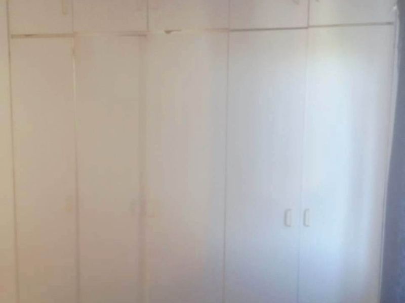 A bedroom featuring floor-to-ceiling built-in cupboards with white cabinetry, showing signs of wear and misalignment.