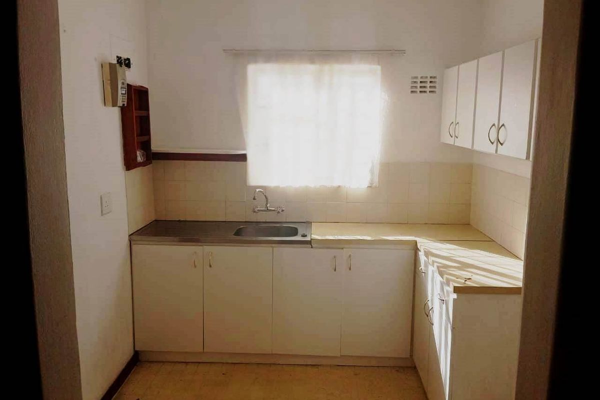 A compact, dated kitchen featuring white built-in cabinetry, a stainless steel sink, and tiled backsplash, offering a functional layout ready for modernization.