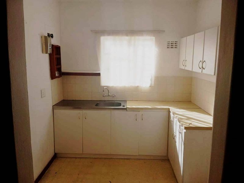 A compact, dated kitchen featuring white built-in cabinetry, a stainless steel sink, and tiled backsplash, offering a functional layout ready for modernization.