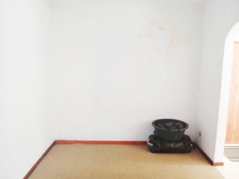 An empty bedroom featuring carpet flooring, timber skirting boards, and an arched doorway, showing signs of wall staining and wear.