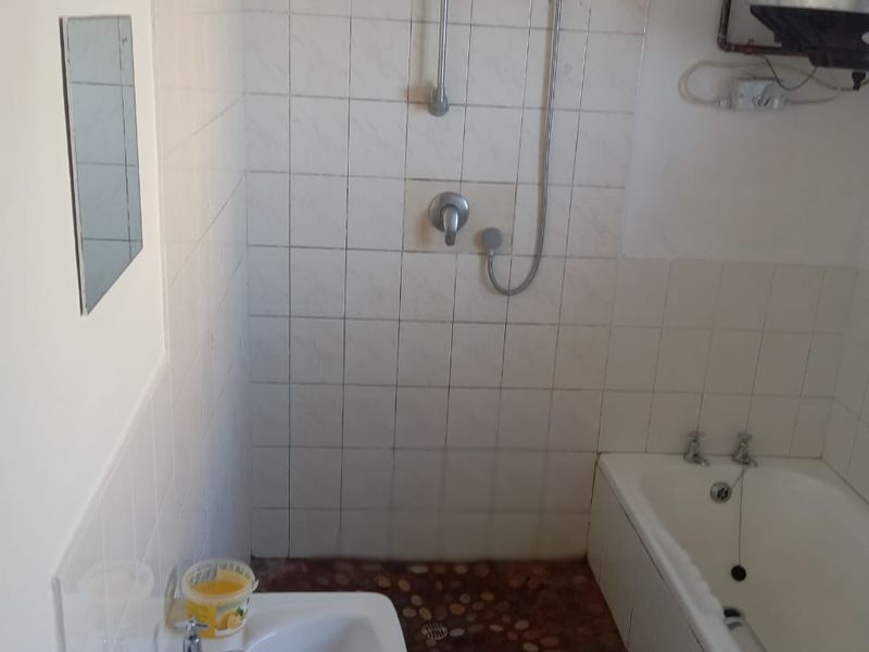 A functional bathroom featuring a bathtub, shower attachment, and basin with tiled walls and a unique pebble-style floor finish.