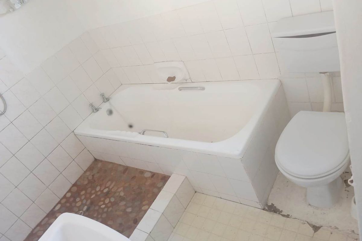 A dated bathroom featuring a built-in bathtub, toilet, and tiled finishes. The space requires renovation to address worn flooring and dated fixtures.