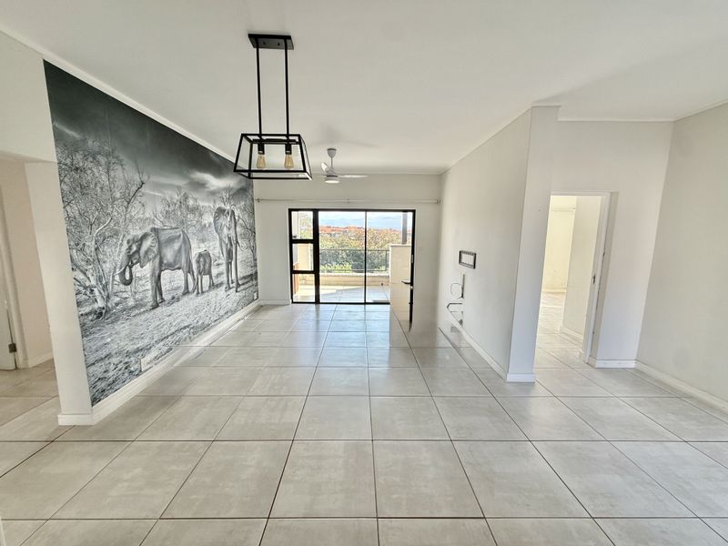 Spacious, light-filled living area featuring large format floor tiles, a modern pendant light, and sliding door access to a balcony with scenic views.