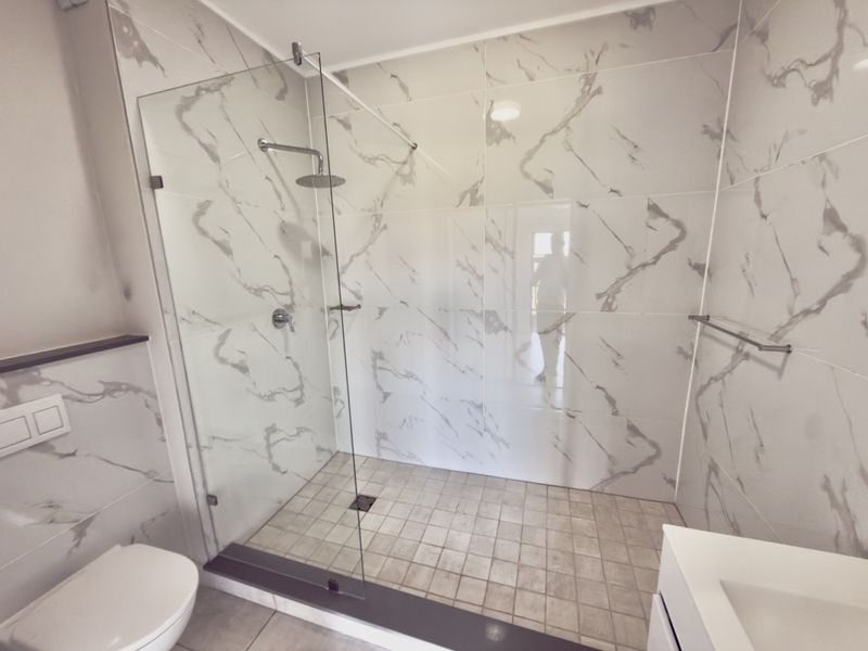 Modern bathroom featuring a spacious walk-in shower with glass screen, rainfall shower head, and elegant marble-look wall tiling.