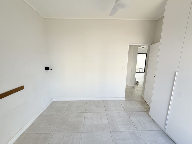An empty bedroom featuring neutral tiled flooring, a built-in wardrobe, and a ceiling fan, offering a clean canvas for personalization.