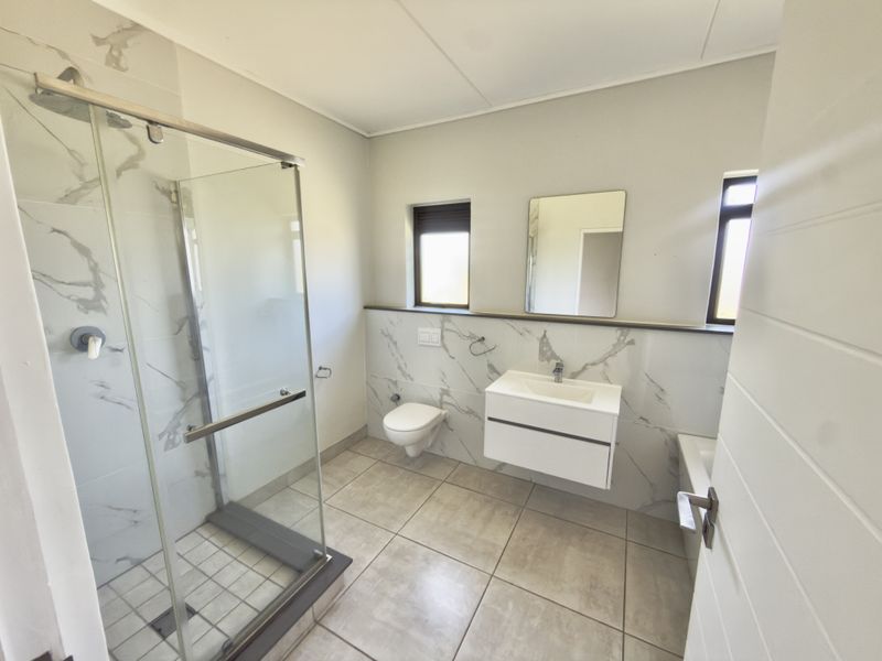 Modern bathroom featuring a glass shower enclosure, wall-mounted toilet, floating vanity, and elegant marble-look wall tiling.