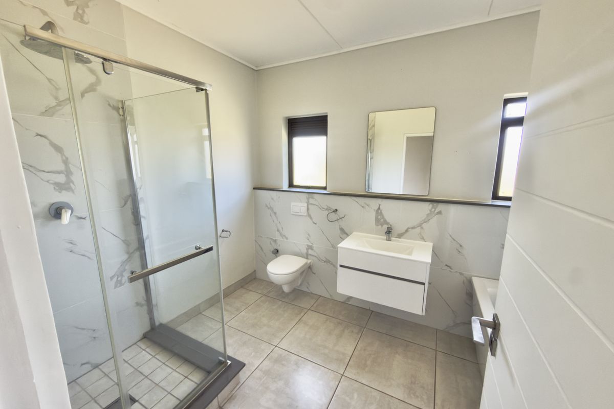 Modern bathroom featuring a glass shower enclosure, wall-mounted toilet, floating vanity, and elegant marble-look wall tiling.