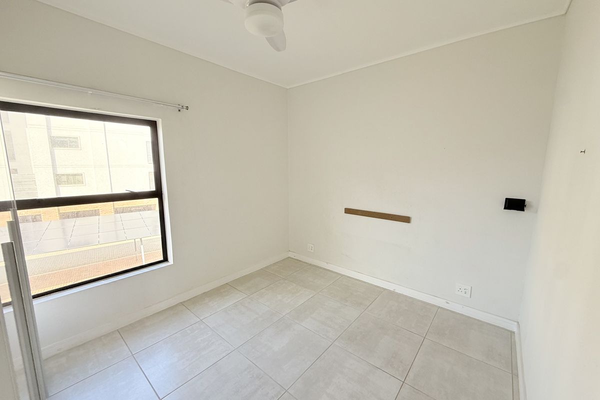 A bright, empty bedroom featuring neutral tiled flooring, a ceiling fan, and large window, providing a clean canvas for personalization.
