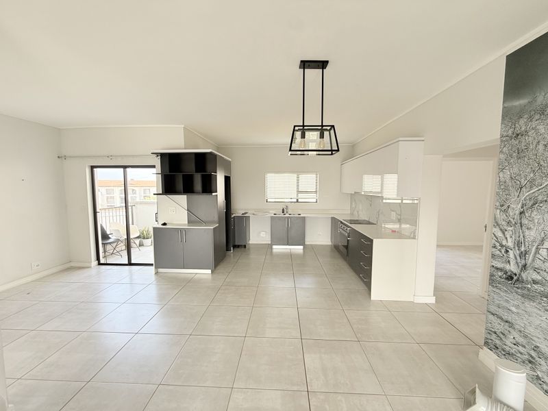 Spacious open-plan kitchen and living area featuring modern cabinetry, tiled flooring, and direct access to a balcony through sliding glass doors.