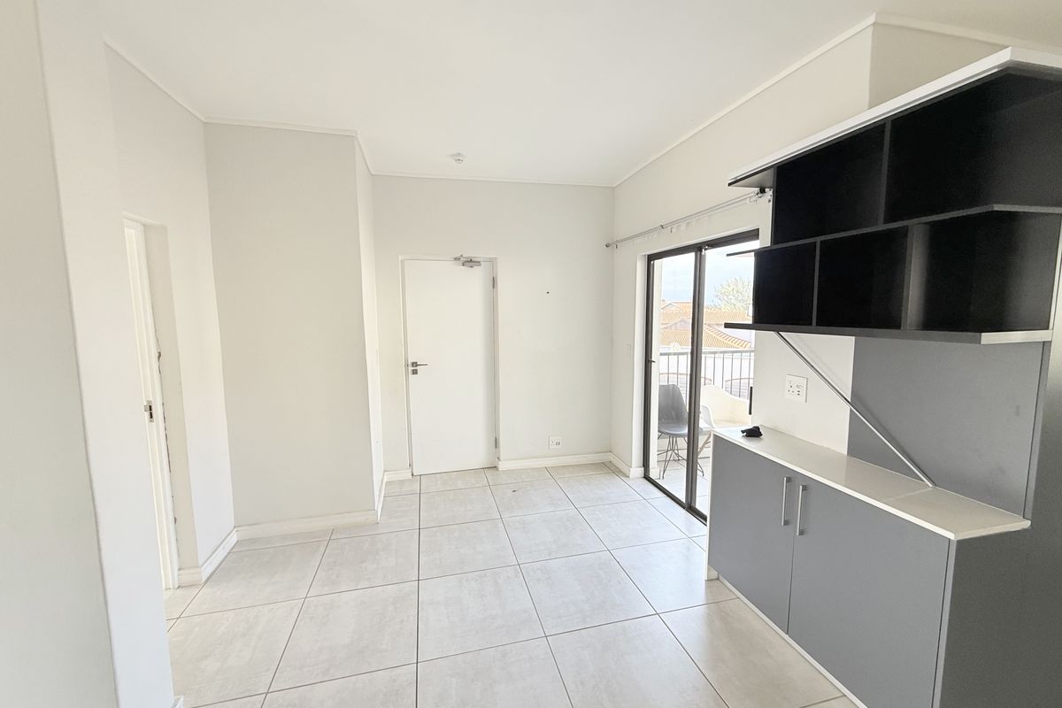 An empty, well-lit living area featuring neutral tiled flooring, modern built-in cabinetry, and direct access to a balcony through sliding glass doors.
