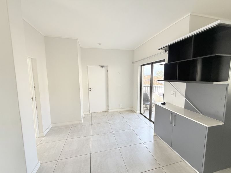 An empty, well-lit living area featuring neutral tiled flooring, modern built-in cabinetry, and direct access to a balcony through sliding glass doors.