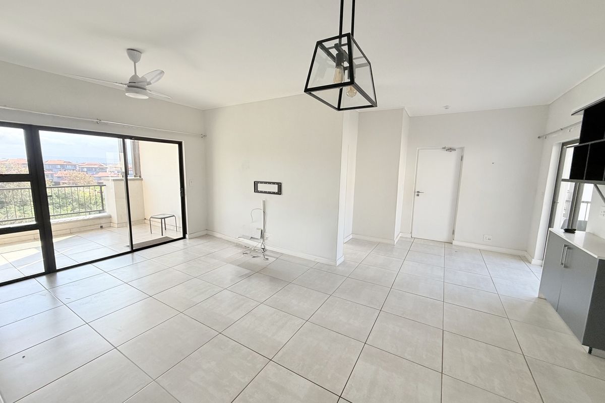 Spacious open-plan living area featuring neutral tiled flooring, modern pendant lighting, a ceiling fan, and large sliding doors leading to a private balcony.