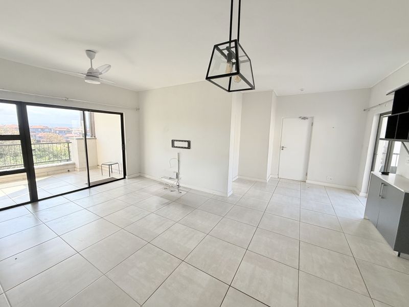 Spacious open-plan living area featuring neutral tiled flooring, modern pendant lighting, a ceiling fan, and large sliding doors leading to a private balcony.