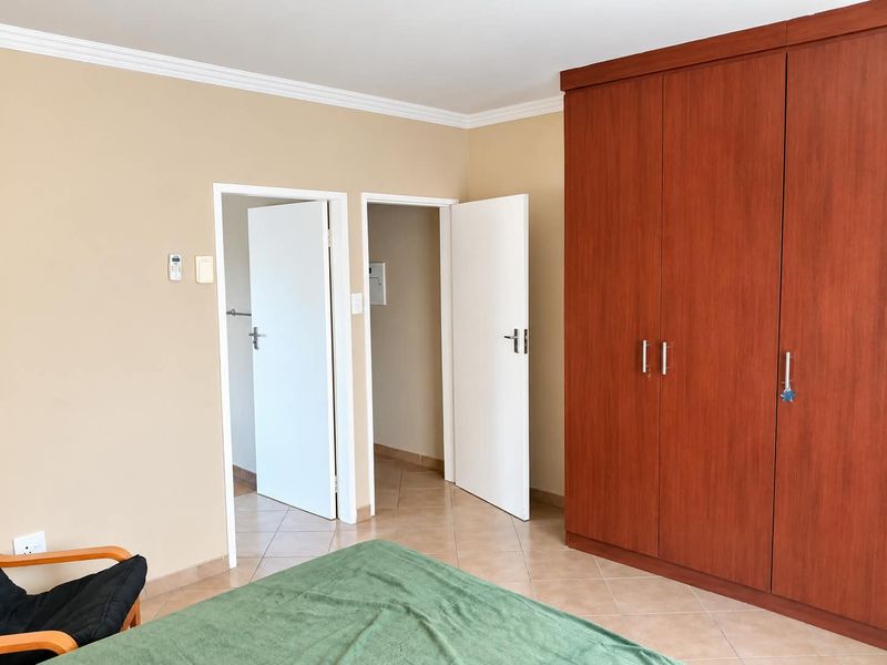 A bedroom featuring tiled flooring, coving, and a large built-in wooden wardrobe, with access to adjacent rooms via internal doors.