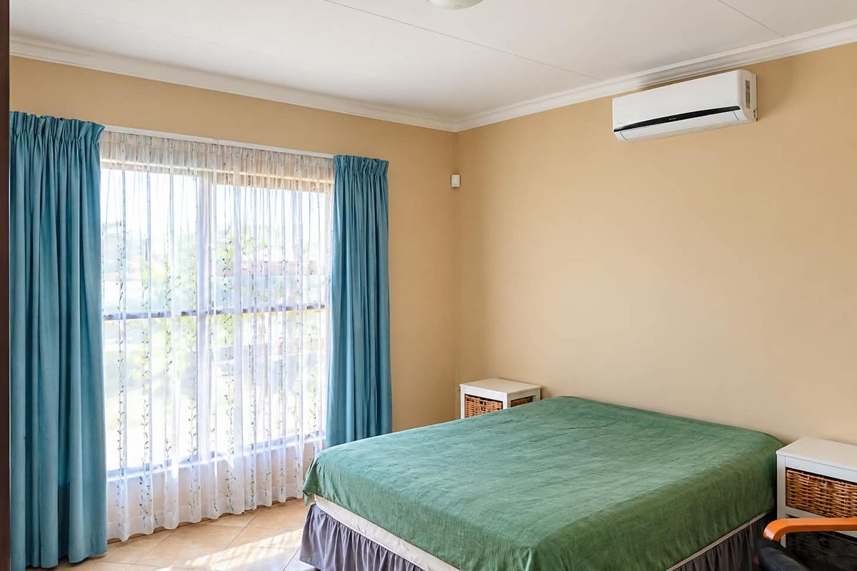 A bedroom featuring tiled flooring, a wall-mounted split-system air conditioner, and large windows with curtains.