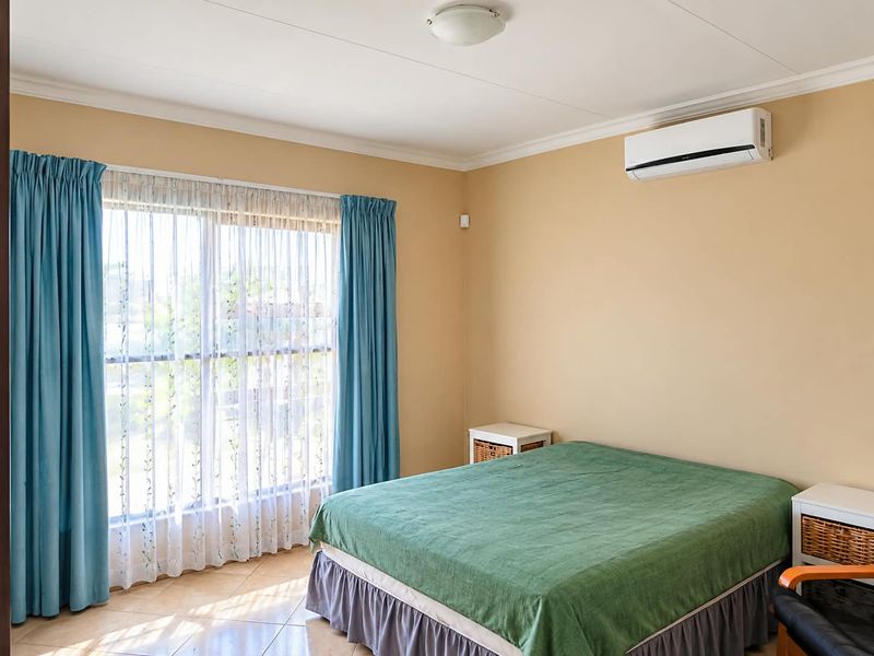 A bedroom featuring tiled flooring, a wall-mounted split-system air conditioner, and large windows with curtains.
