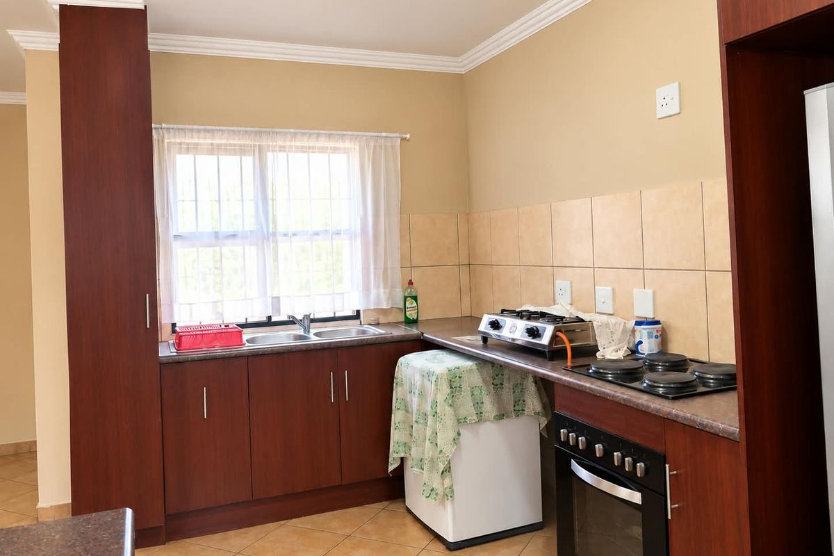 A functional kitchen featuring dark wood cabinetry, laminate countertops, tiled backsplash, and built-in oven with electric hob.