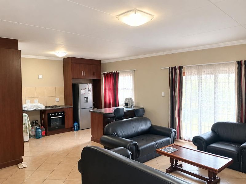 Open-plan living area featuring a kitchen with built-in cabinetry, oven, and hob, flowing into a lounge space with sliding door access to the exterior.
