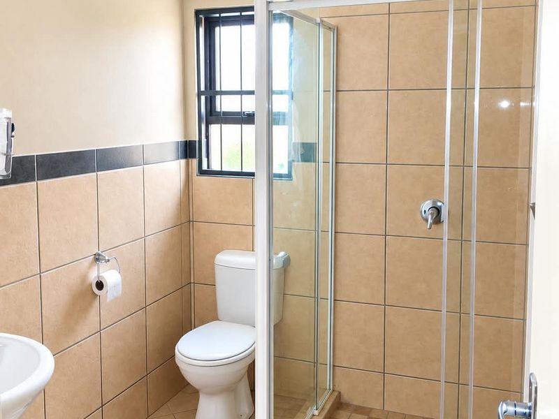 A functional bathroom featuring a glass-enclosed shower, pedestal basin, and toilet with neutral-toned wall and floor tiling.