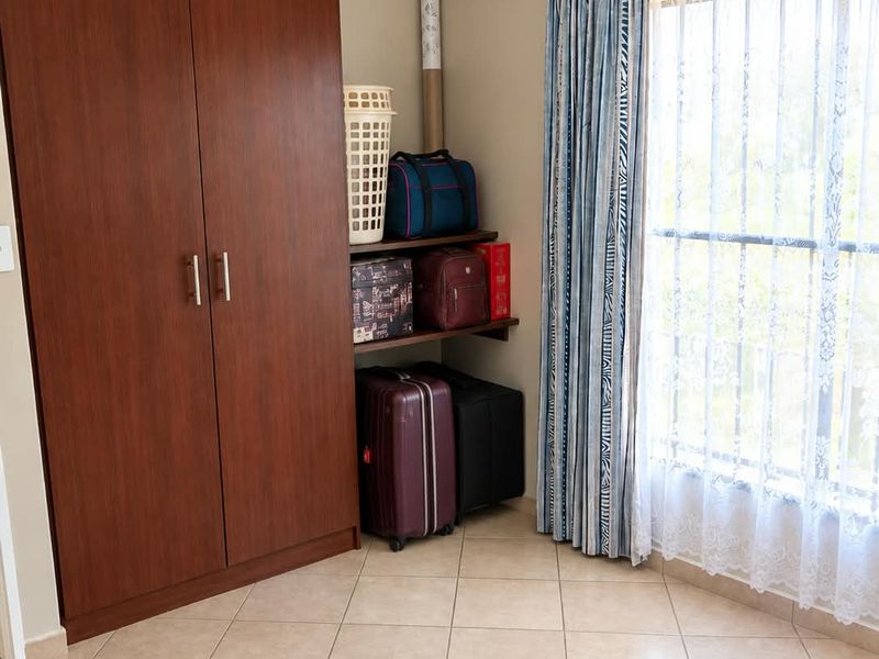 A bedroom featuring tiled flooring and a built-in wooden wardrobe, offering functional storage space and natural light through the window.