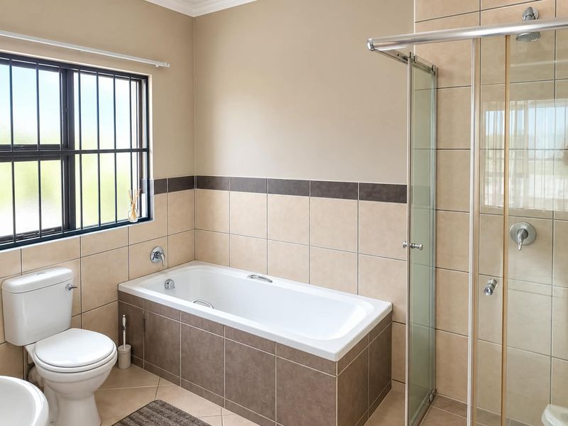 A clean, functional bathroom featuring a built-in bathtub, a separate glass-enclosed shower, and neutral ceramic tiling throughout.