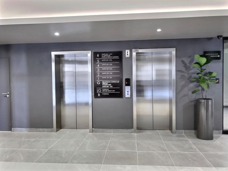 Modern apartment building elevator lobby featuring stainless steel lift doors, clear floor directory signage, and neutral tiled flooring.