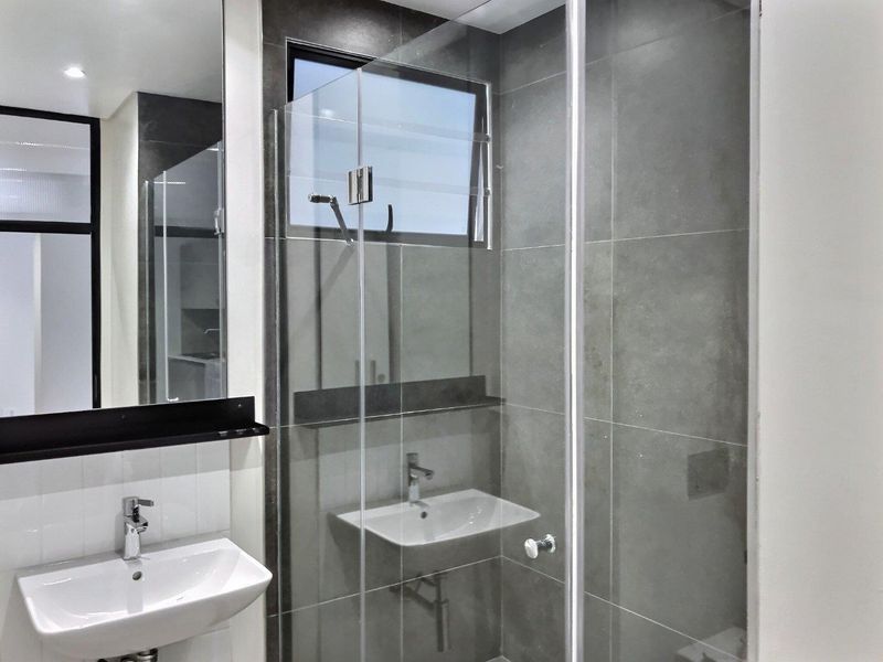 Modern bathroom featuring a glass-enclosed shower, wall-mounted basin with chrome fixtures, and contemporary large-format grey wall tiling.
