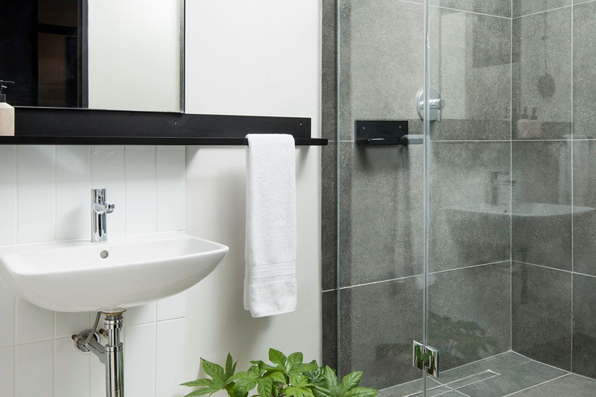 Modern bathroom featuring a wall-mounted basin, sleek chrome fixtures, and a contemporary glass-enclosed shower with grey tiled finishes.