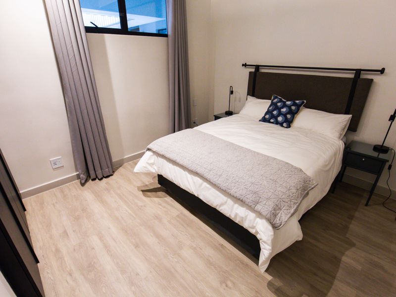 A modern bedroom featuring light-toned laminate flooring, neutral walls, and a built-in wardrobe, offering a clean and contemporary living space.